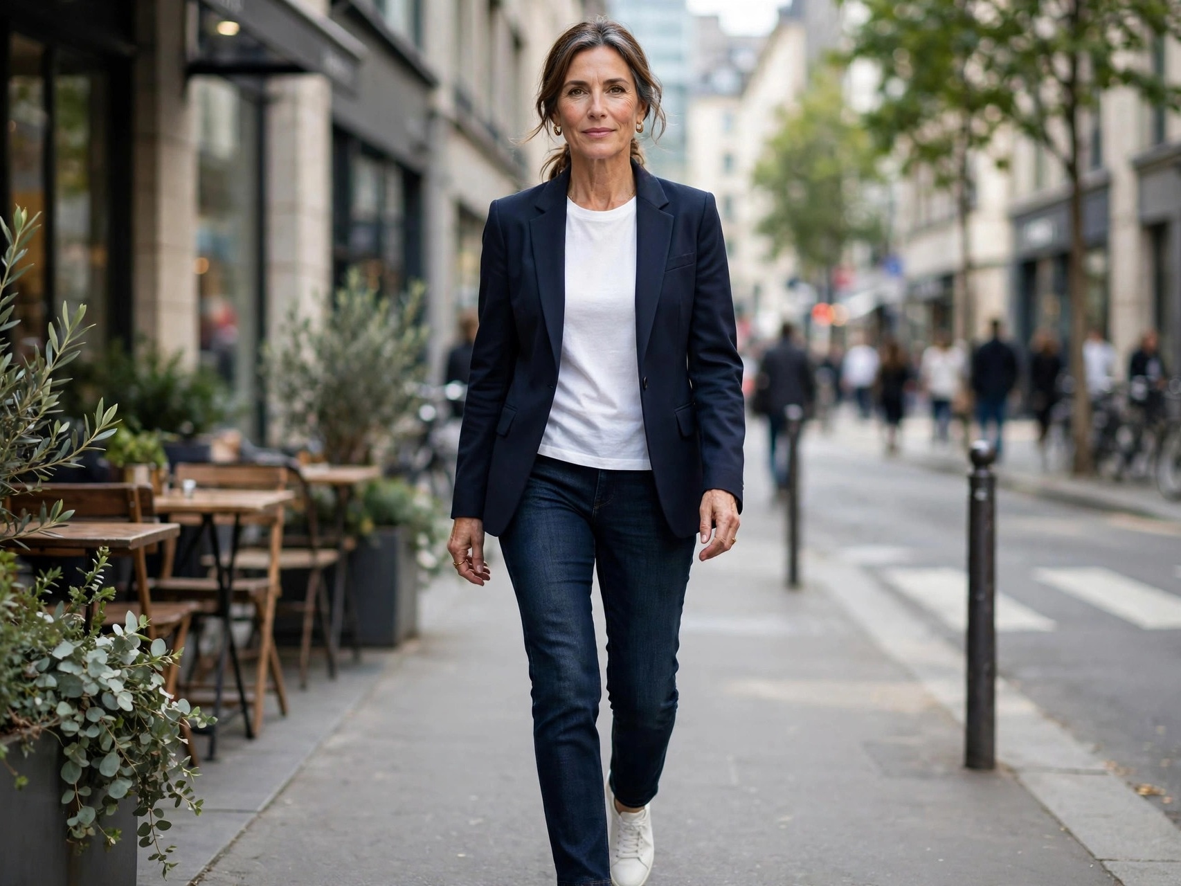 Confident 50-year-old woman in a chic blazer and jeans walking on a city street