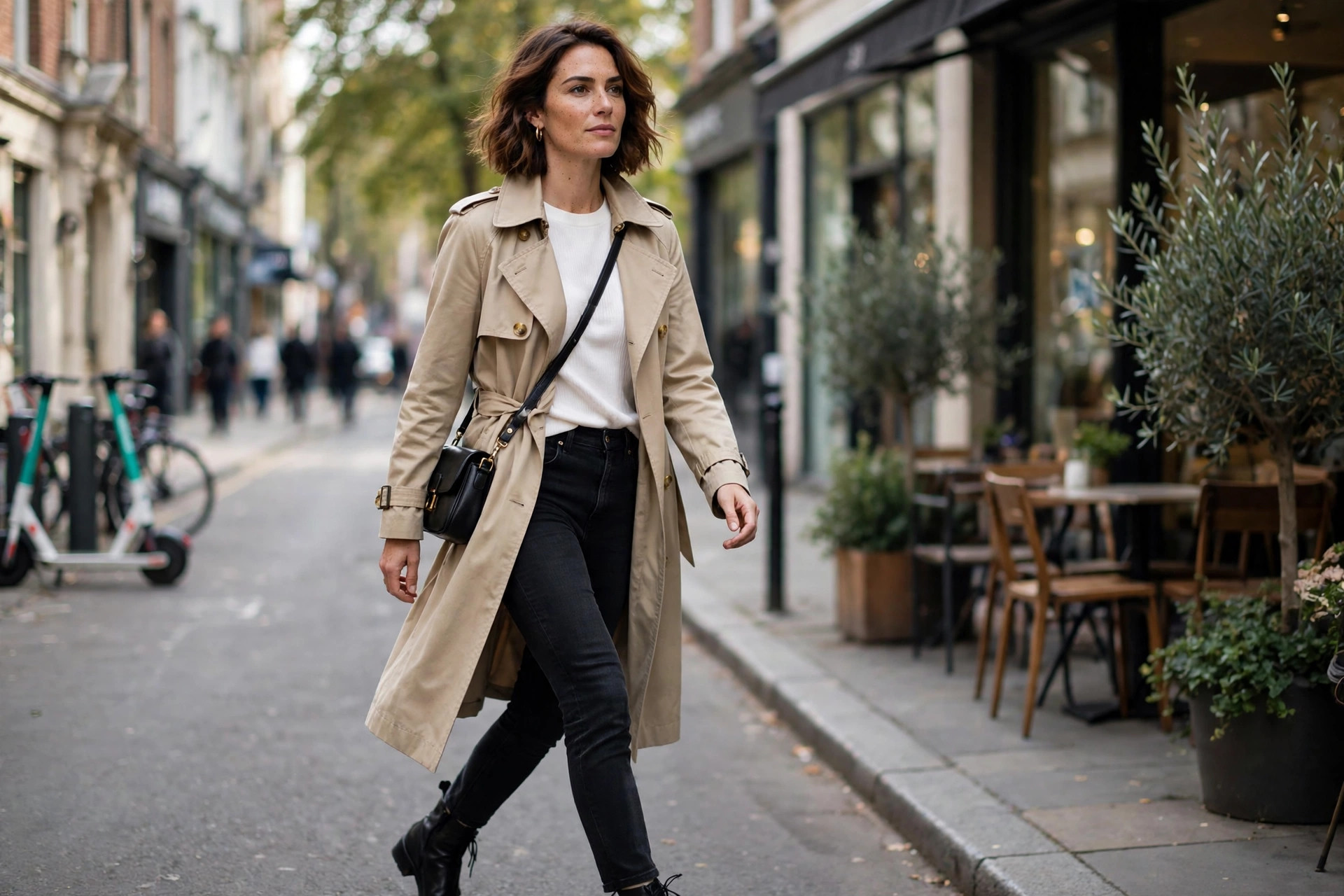 Confident 30-year-old woman in a chic trench coat and ankle boots walking on a city street