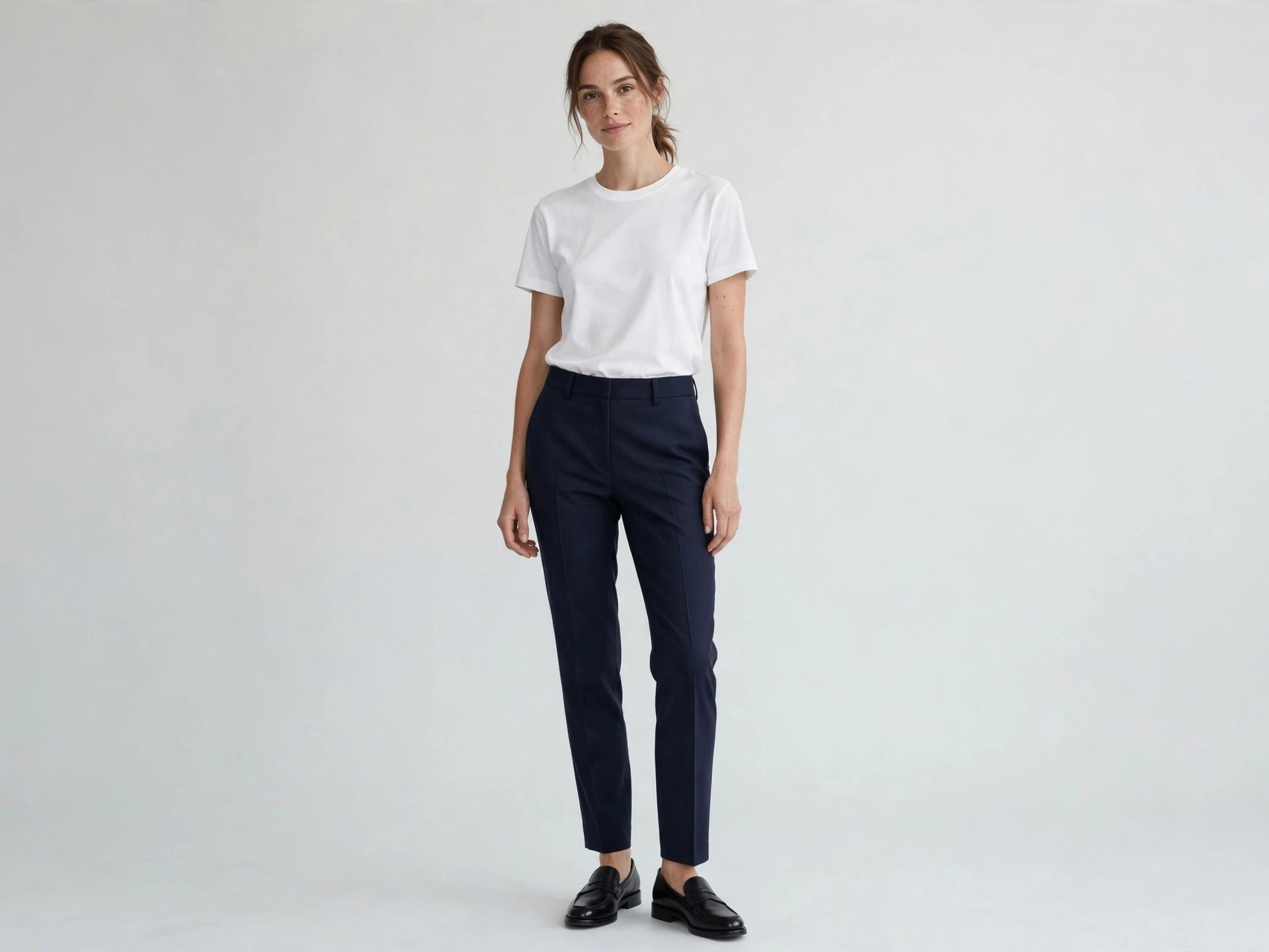 Woman wearing elevated basics: fitted white cotton t-shirt with tailored navy trousers and loafers, minimalist outfit for 30-year-old women